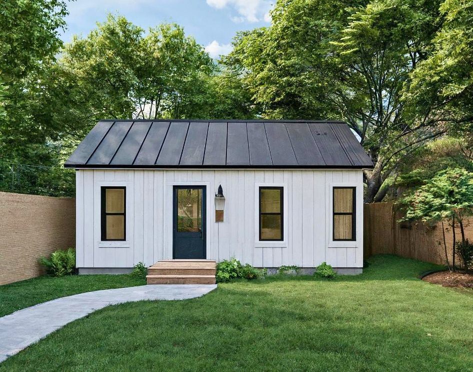 Are Manufactured Homes Considered Real Estate - Small white ADU with black metal roof in a landscaped backyard.