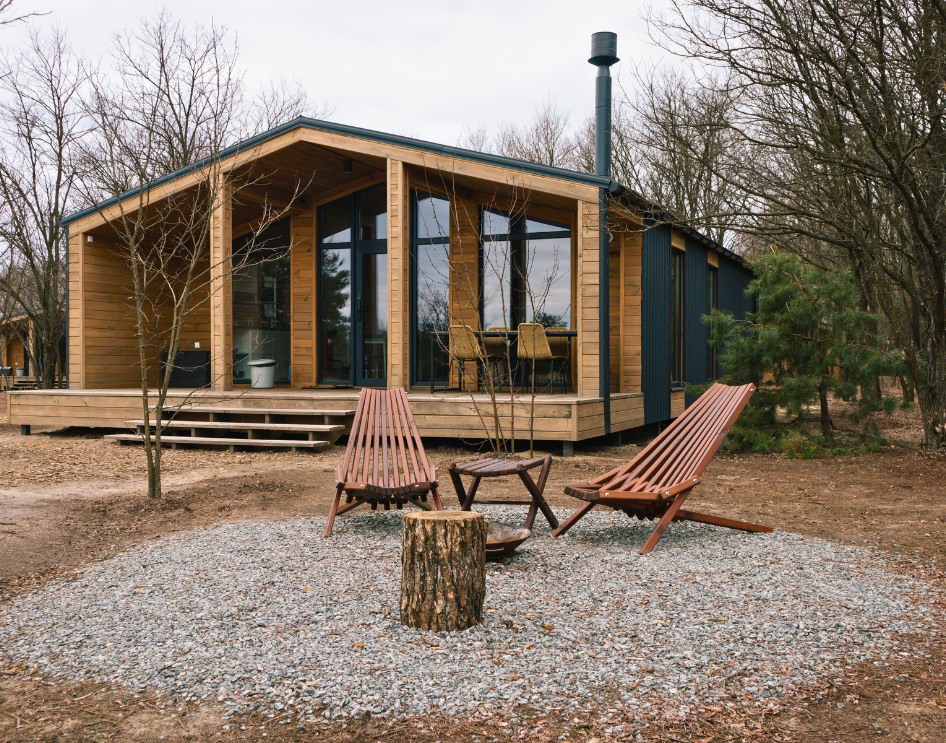 Why Do People Choose to Buy Manufactured ADUs - Wooden prefab ADU in a birch forest with large windows.